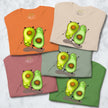 Five folded Avocado Yoga Tees in cream white, sage green, matcha green, rosewood, and orange, each featuring two cute yoga‑posing avocado characters.
