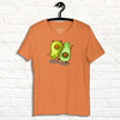 Orange  yoga shirt on a hanger, showing a playful yoga‑avocado illustration with bold contrast and energetic, sporty tones.