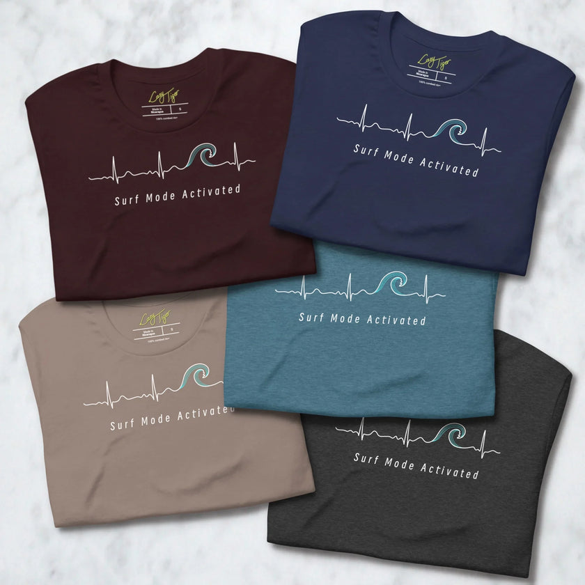 Folded Surf Mode Activated Tees in all five available colors, each displaying the heartbeat‑wave line art and ‘Surf Mode Activated’ text.