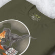 Folded olive green T‑shirt with detailed Pizza Raptor print, closeup of dinosaur and pizza artwork on comfy unisex tee.