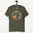 Olive green graphic tee on hanger featuring a playful pizza‑stealing raptor holding a slice of pizza, funny dinosaur T‑shirt for adults and teens.
