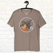 Taupe neutral T‑shirt on hanger showing a cartoon raptor grabbing pizza, funny foodie dinosaur graphic tee.