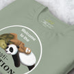Detailed view of folded sage green tee showing the Procrasti‑NATION sloth, panda, and turtle illustration with soft minimalist lines.
