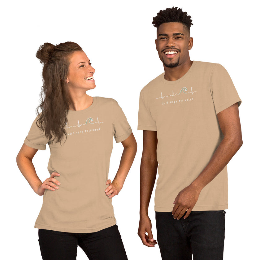 Model wearing the beige Heartbeat Surf Tee with the minimalist ECG‑inspired heartbeat‑wave graphic and ‘Surf Mode Activated’ text, styled in a bright, summery coastal look