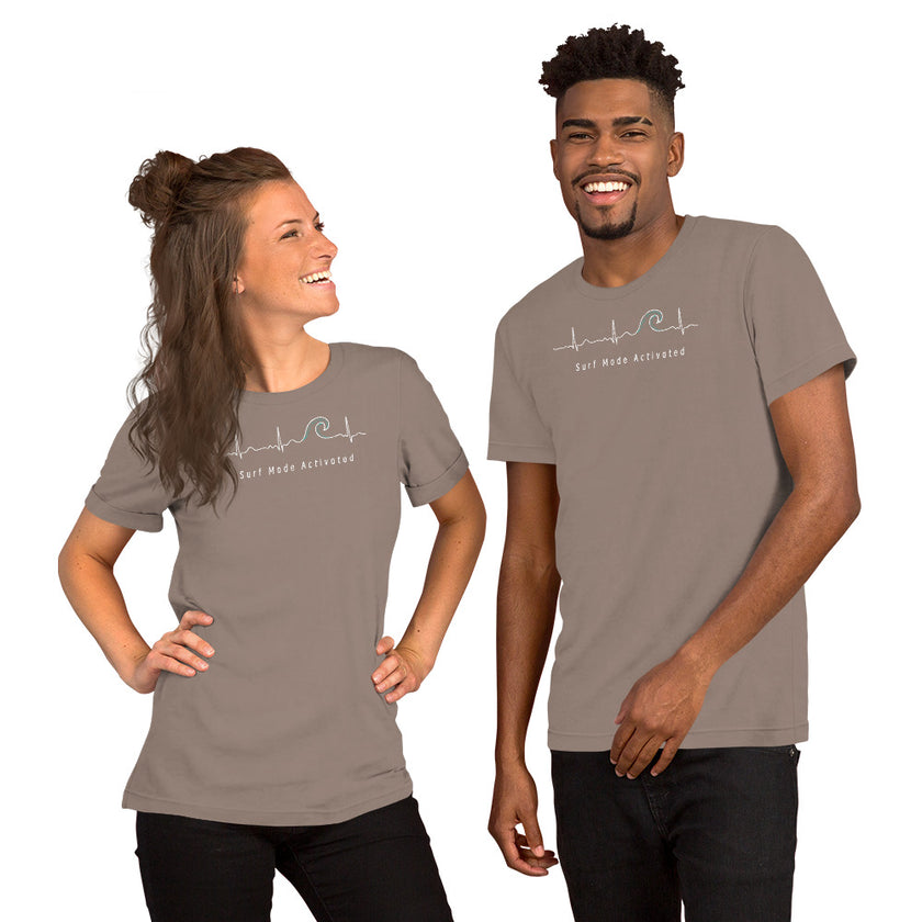 Model wearing the taupe Heartbeat Surf Tee with the ECG‑style heartbeat‑wave surf design and ‘Surf Mode Activated’ text, creating a warm neutral surf‑lifestyle aesthetic