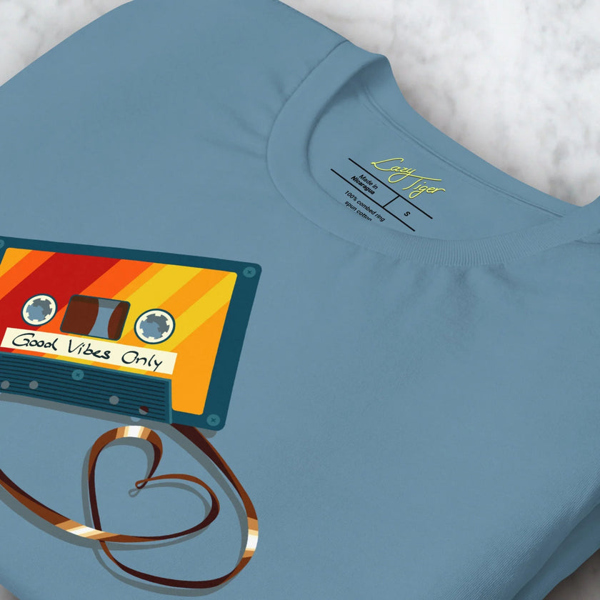 Close-up detail of a folded denim blue Retro Vibes Cassette Tee, highlighting the colorful cassette illustration and heart‑shaped tape.